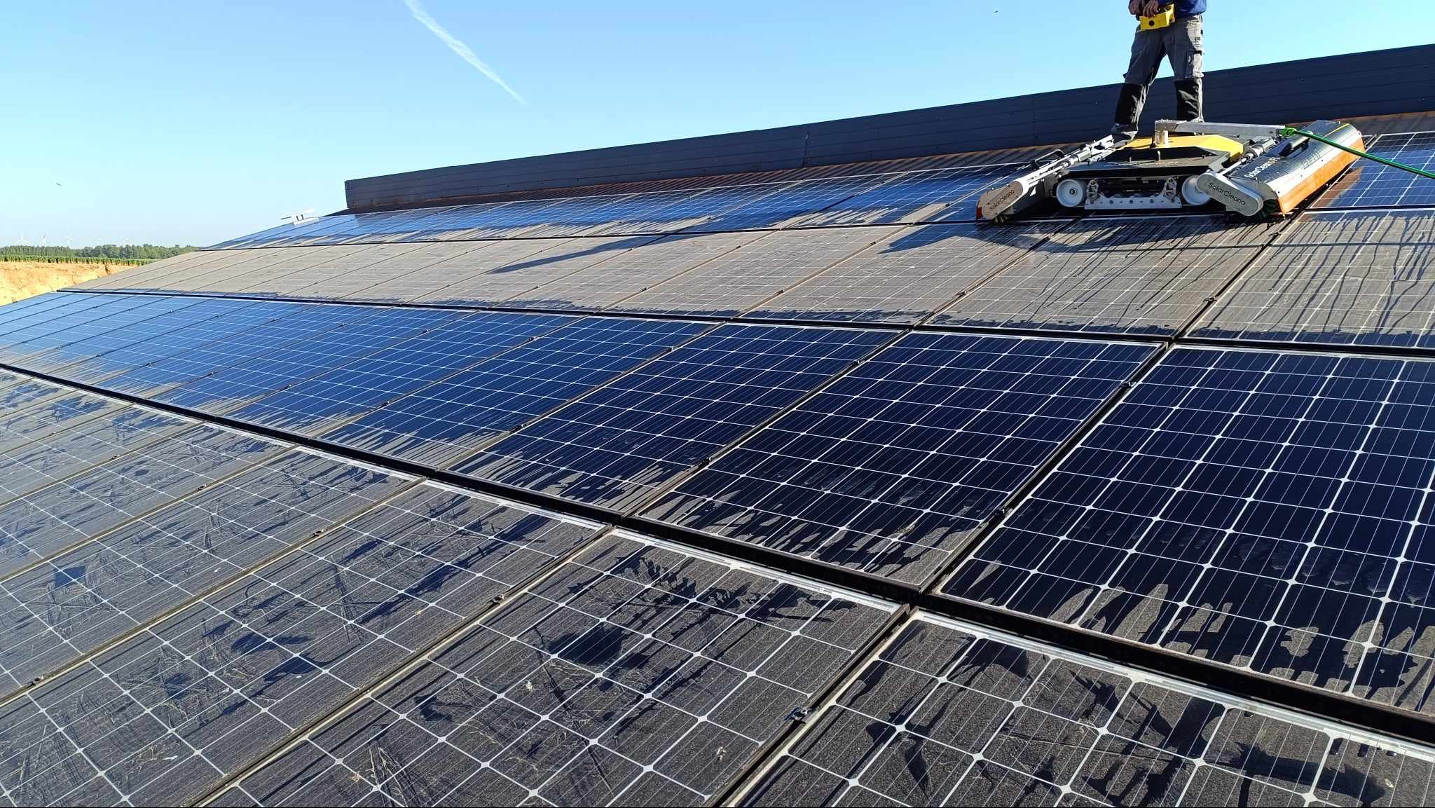 Czyszczenie paneli fotowoltaicznych na dachu za pomocą robota czyszczącego, widoczne ślady wody i czyste panele po przejeździe urządzenia.