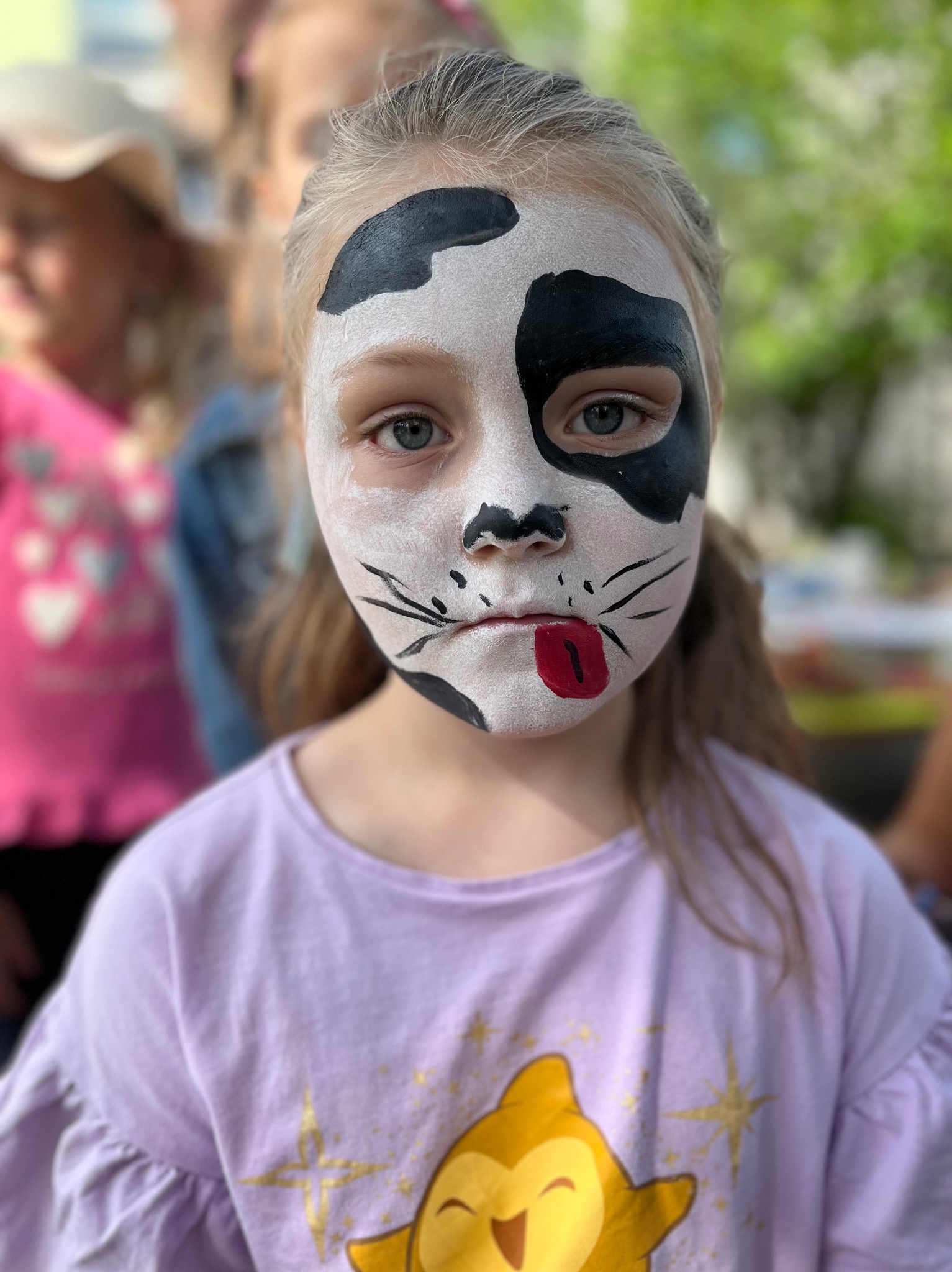 Dziewczynka z pomalowaną twarzą w stylu krowy i kota podczas imprezy w Koninie, na tle innych dzieci.