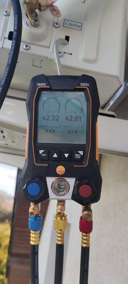 Manometr cyfrowy Testo 550s podłączony do instalacji klimatyzacyjnej, wskazujący ciśnienie 42.32 i 42.61 bar, z widocznymi przewodami w kolorach niebieskim, żółtym i czerwonym.