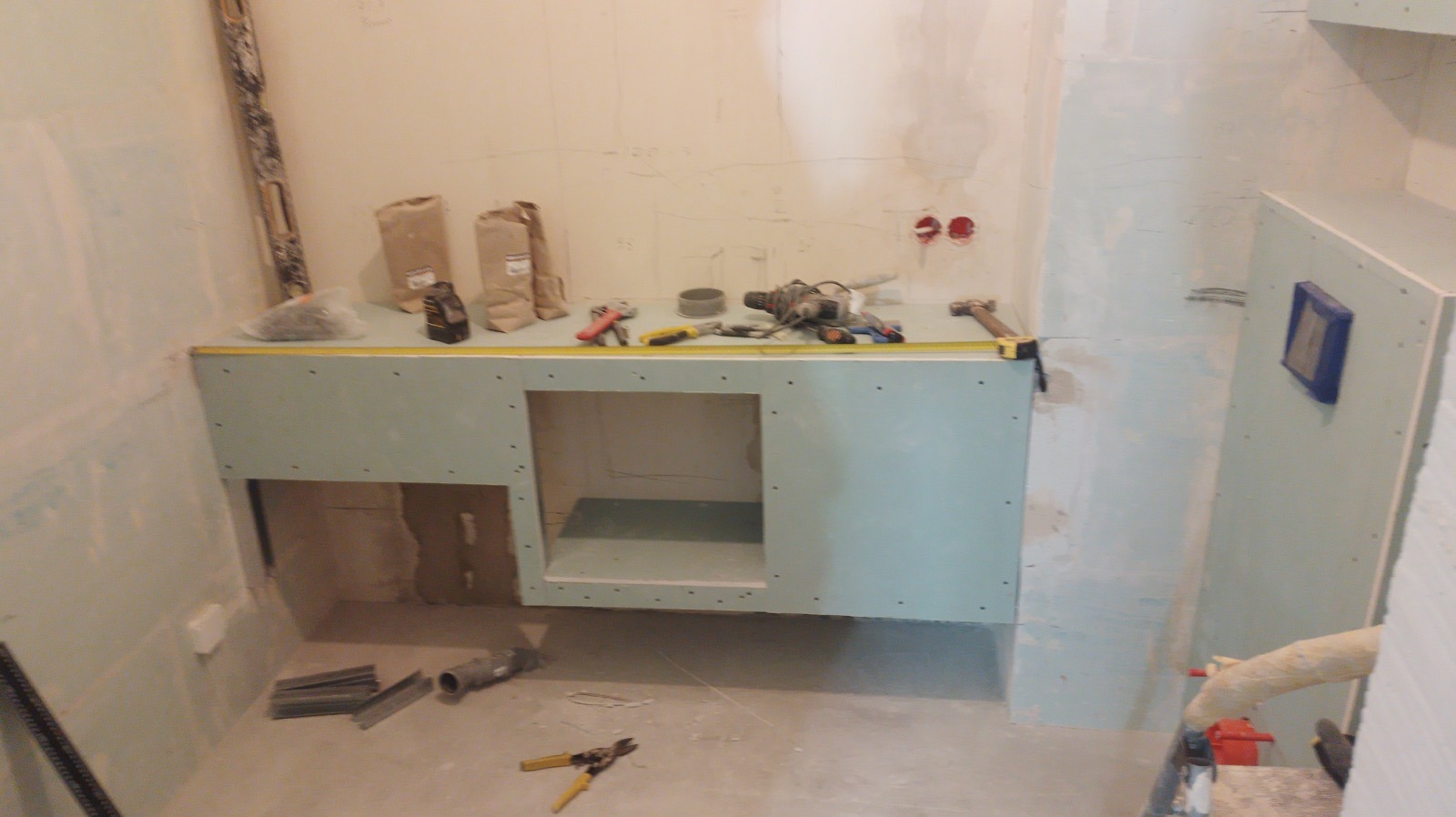Niedokończona zabudowa z płyt gipsowo-kartonowych w łazience, widoczne narzędzia, worki z zaprawą, puszki elektryczne w ścianie