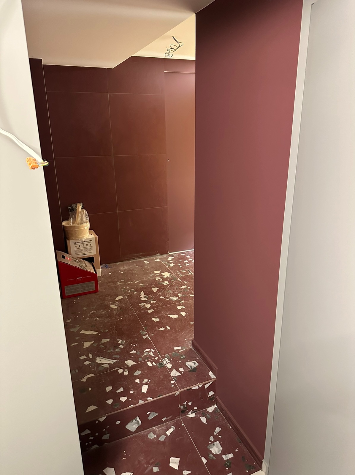 Korytarz w trakcie układania terakoty w kolorze bordo z białymi wstawkami, widoczne narzędzia i materiały budowlane.