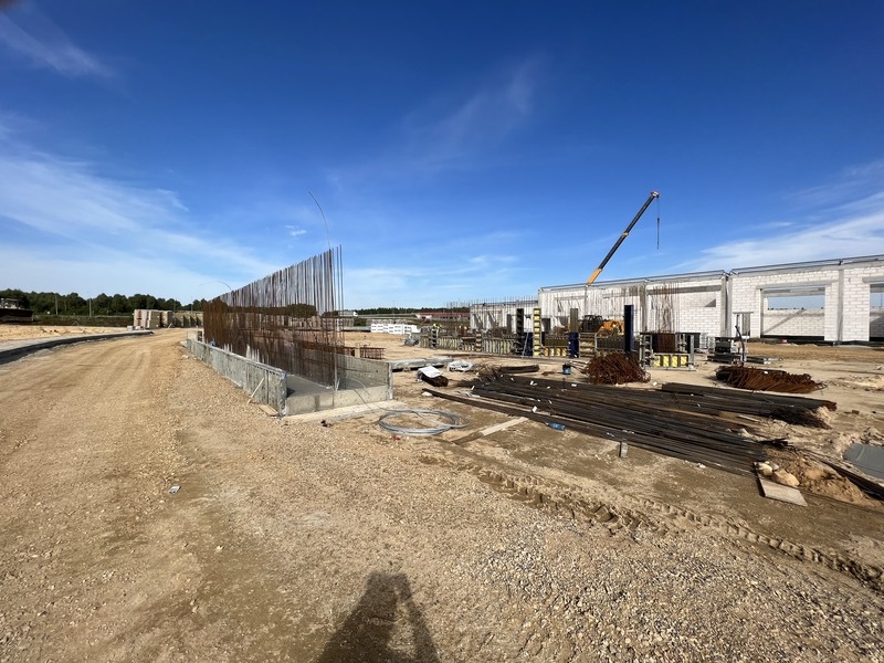 Budowa hali: zbrojenie fundamentów, ściany z bloczków, żuraw na tle błękitnego nieba.