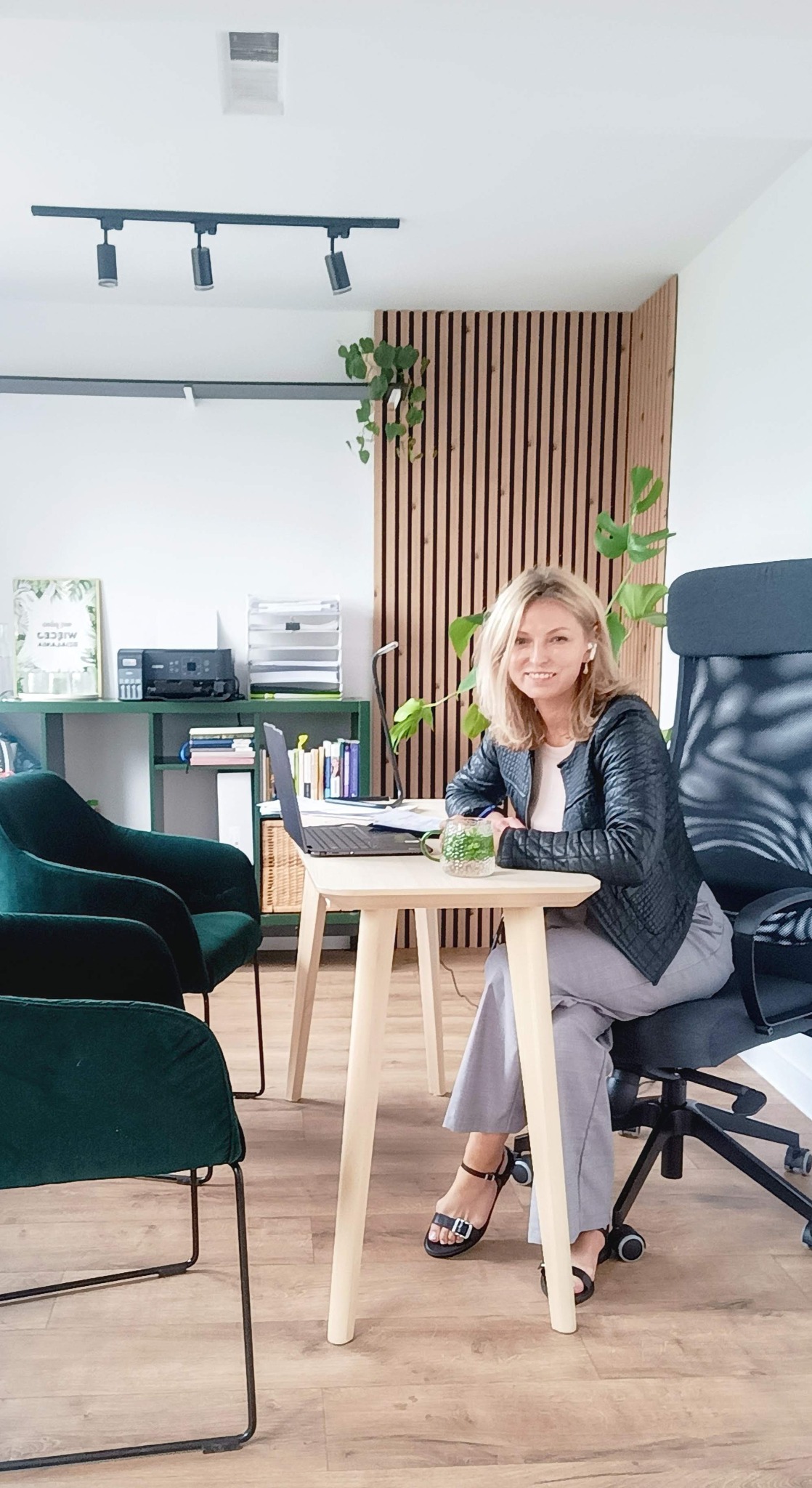 Profesjonalistka w czarnej kurtce siedzi przy jasnym biurku z laptopem w nowocześnie urządzonym biurze.