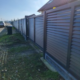 Montaż ogrodzeń Adam Andrzejewski - Długa, nowoczesna, pozioma, szara przesłona z metalu, tworząca ogrodzenie posesji, widoczna z zewnątrz, z domem w tle.