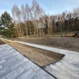 Brukowanie Łukasz Kosz - Układanie kostki brukowej na posesji z wybrukowanymi schodami i ścieżką, w tle krajobraz z drzewami i pracujący mały żółty koparka.