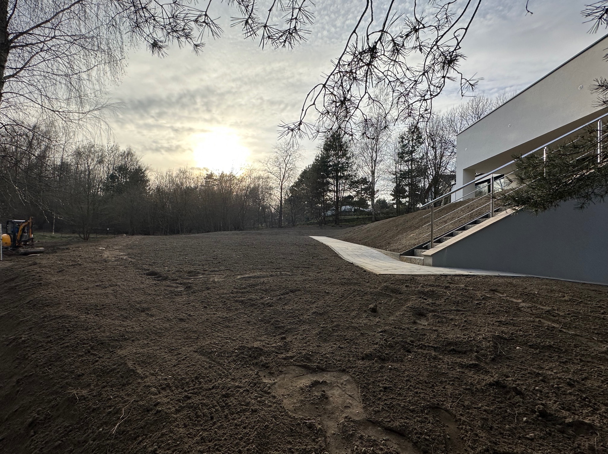 Przygotowany teren pod trawnik w Czyżowicach po niwelacji, z widocznymi śladami opon i świeżo ułożonym chodnikiem prowadzącym do nowoczesnego budynku.