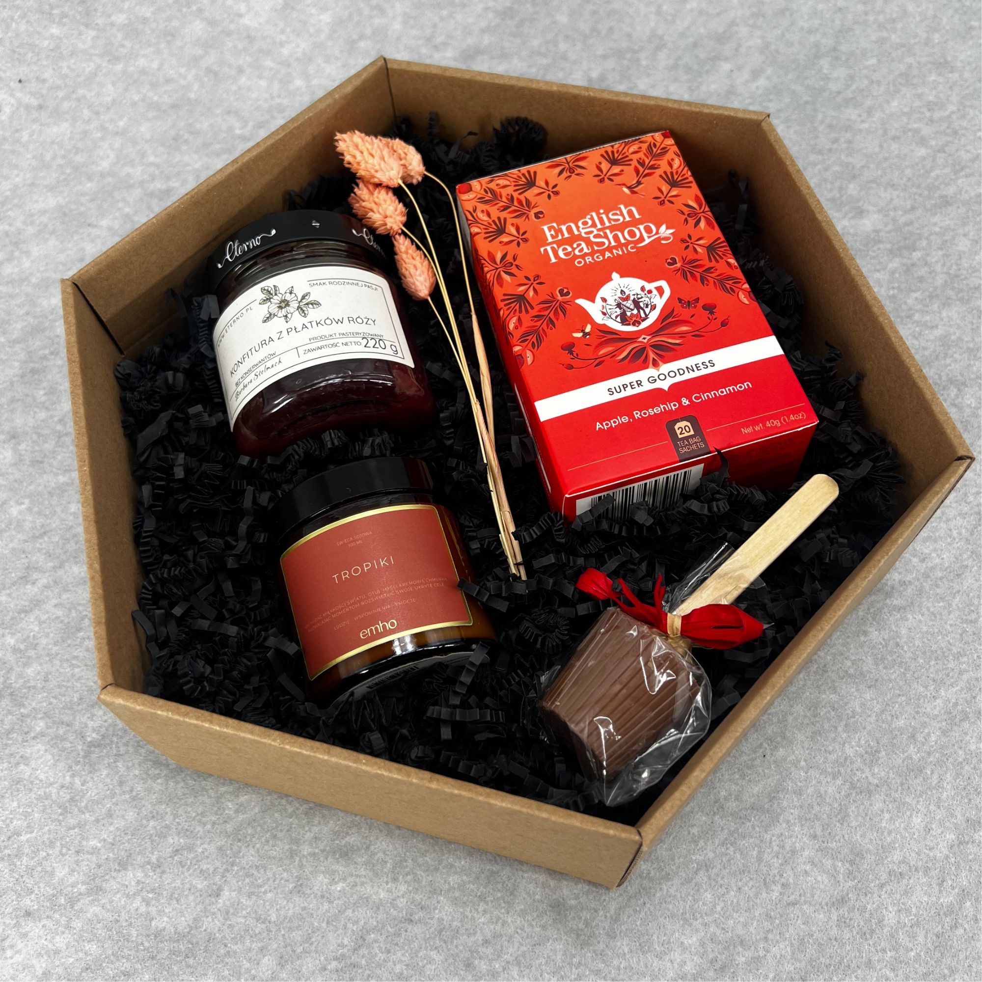 Zestaw upominkowy w brązowym pudełku z czarnym wypełniaczem, zawierający konfiturę z płatków róży, sojową świecę o zapachu tropikalnym, herbatę English Tea Shop o smaku jabłka, róży i cynamonu...