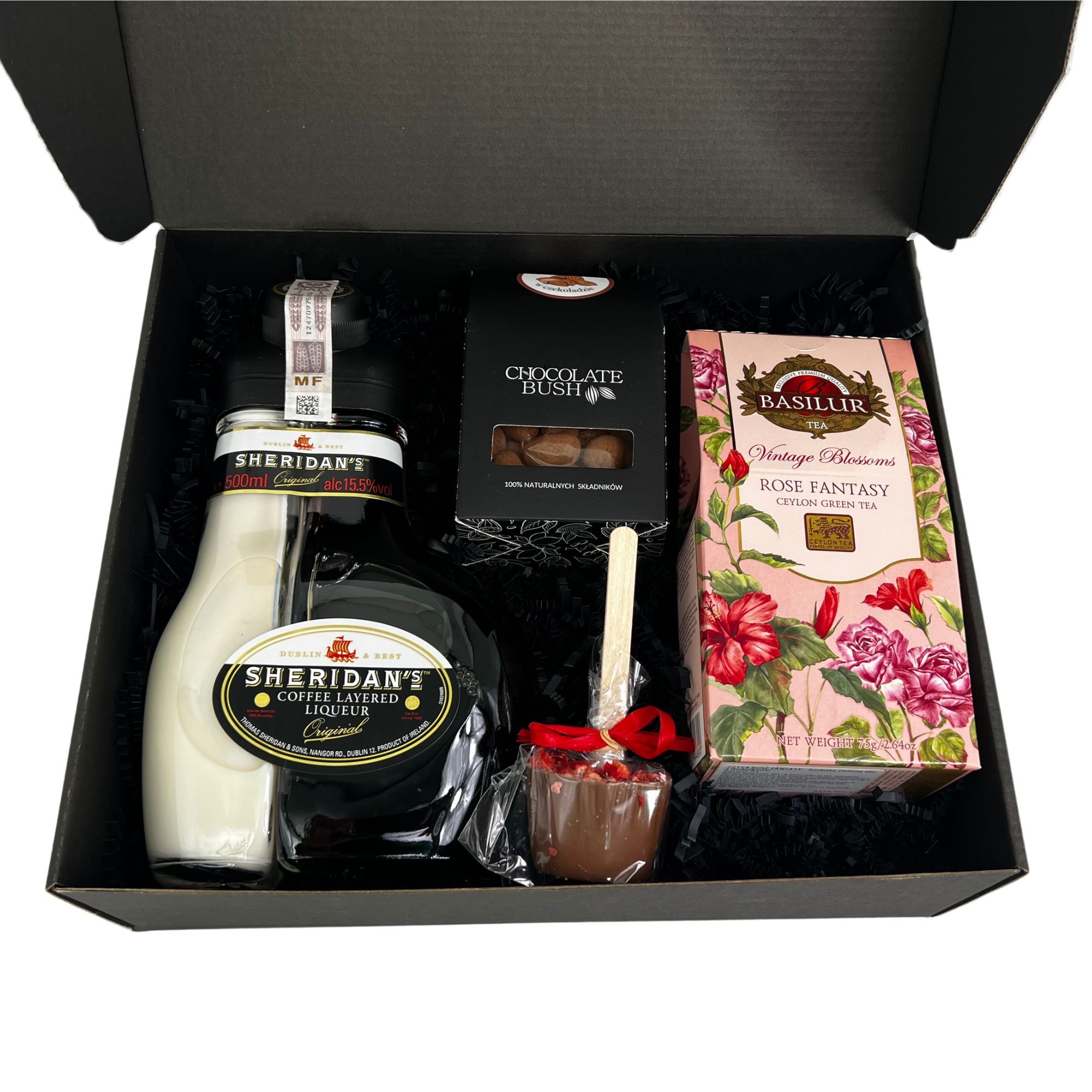 Czarny kartonowy box wypełniony czarnym sizalem, zawierający butelkę likieru Sheridan's, pudełko czekoladek Chocolate Bush, herbatę Basilur Rose Fantasy oraz czekoladowy kubeczek z czerwoną wstążką.