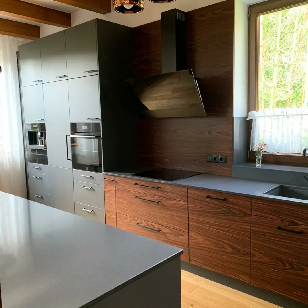 Nowoczesna kuchnia z drewnianymi frontami szafek dolnych i szarymi szafkami górnymi, czarny okap podszafkowy i wyspa kuchenna z szarym blatem.