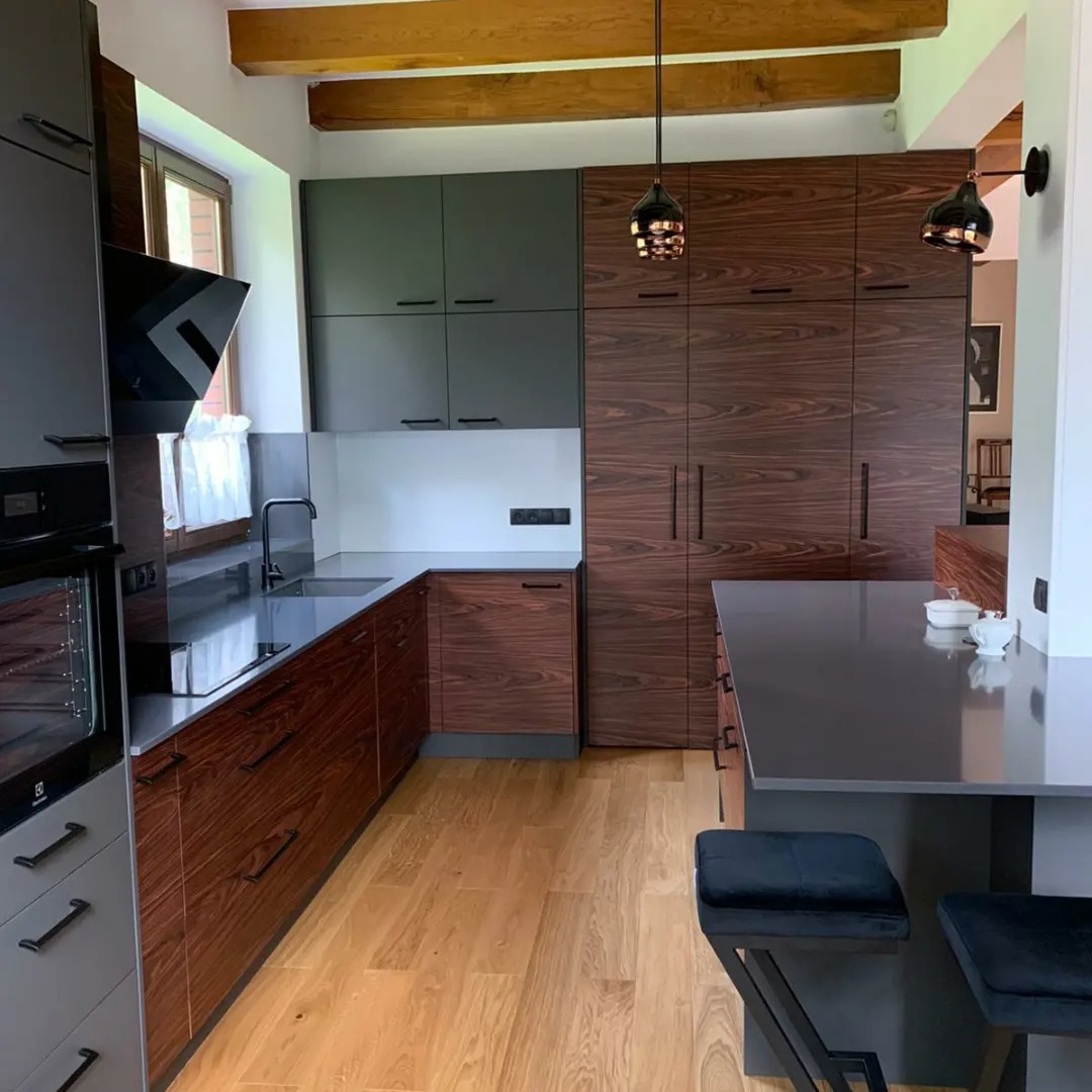 Nowoczesna kuchnia w Ciechocinie z drewnianymi frontami szafek dolnych i szarymi górnymi, czarny blat i wyspa kuchenna z hokerami, oświetlenie punktowe.