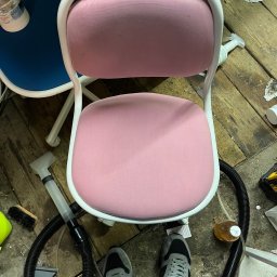 Łukasz Rusiński LukClean - Widok z góry na różowe krzesło z białą ramą, obok sprzęt czyszczący, w tym ssawka odkurzacza i szczotka, na podłodze z desek