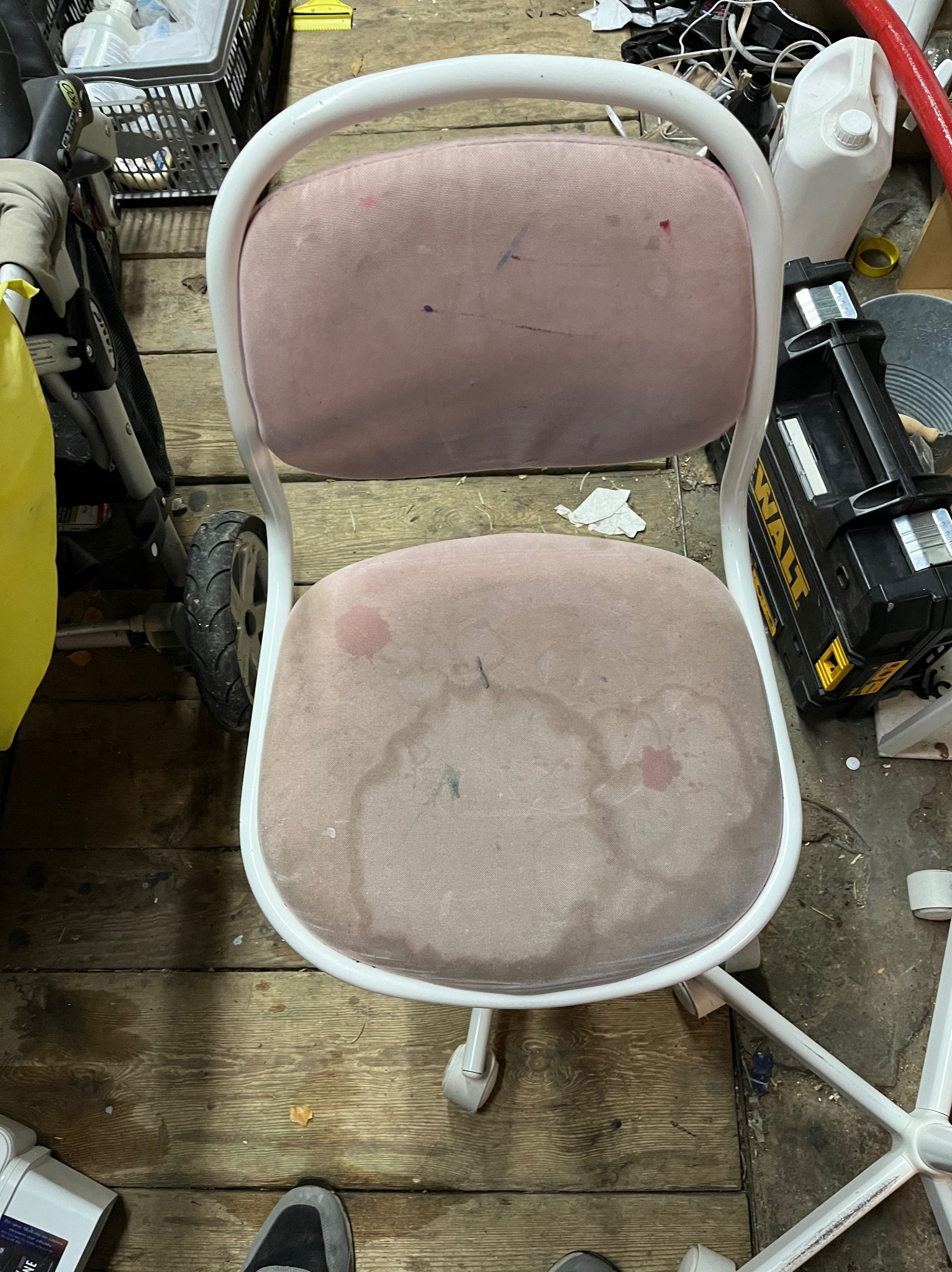 Brudne, różowe krzesło biurowe na kółkach, z plamami na tapicerce, sfotografowane w Lublinie na tle drewnianej podłogi w warsztacie, obok narzędzi i akcesoriów.