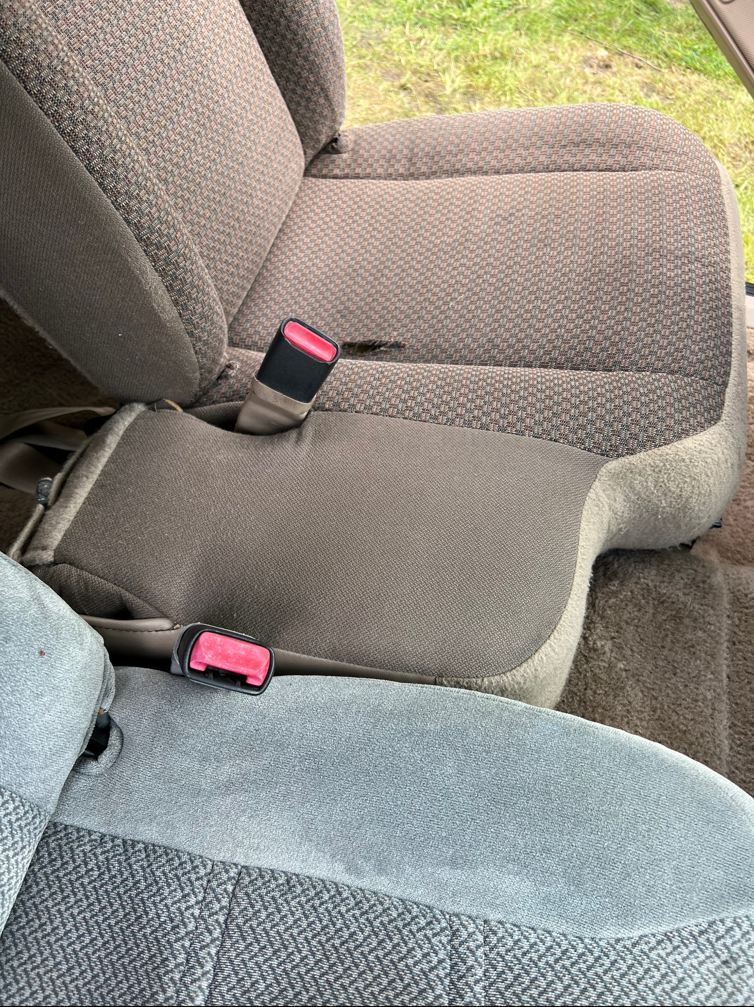 Dwa fotele samochodowe z różną tapicerką: brązowo-beżowa krata na górnym fotelu i szaro-niebieski wzór zygzakowaty na dolnym, oba z widocznymi elementami pasów bezpieczeństwa.