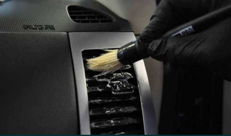 Czyszczenie szczotką wentylacji samochodowej z widoczną pianą czyszczącą i rękawicą ochronną.