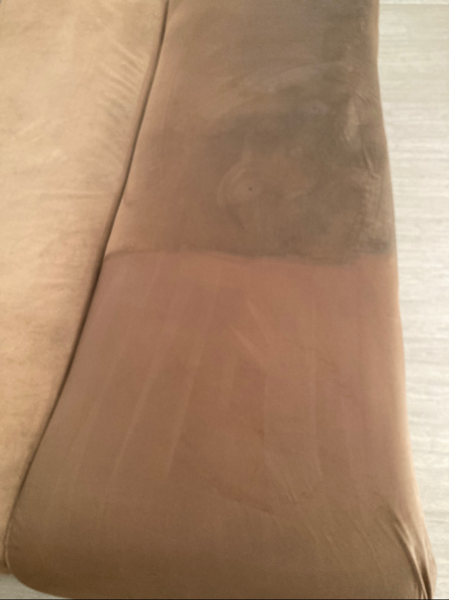 Fragment beżowej tapicerki meblowej, widoczna wyraźna różnica w czystości między górną, brudną częścią a dolną, wyczyszczoną strefą.