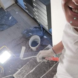 Karol Bal - Malarz na schodach w trakcie prac, widoczny wałek, wiadro z farbą i lampa oświetleniowa