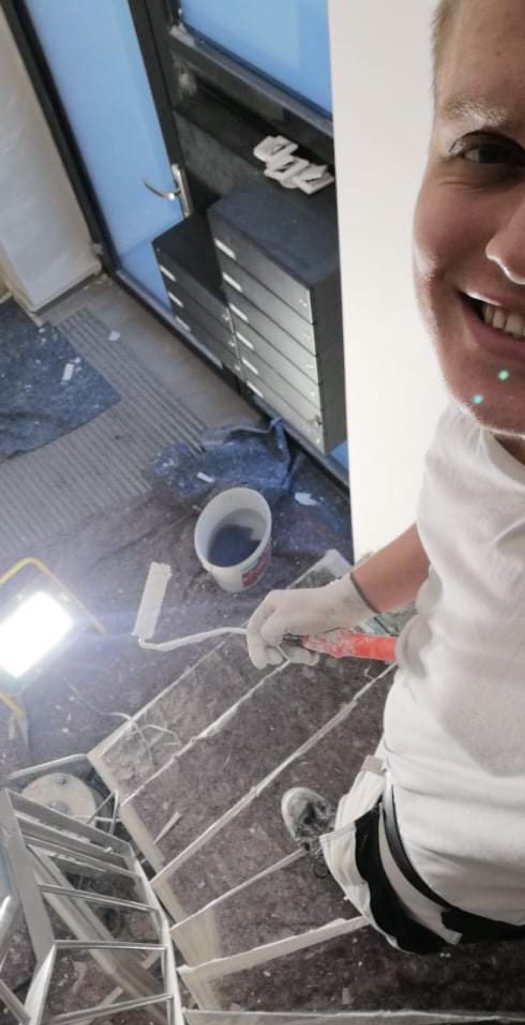 Malarz na schodach w trakcie prac, widoczny wałek, wiadro z farbą i lampa oświetleniowa