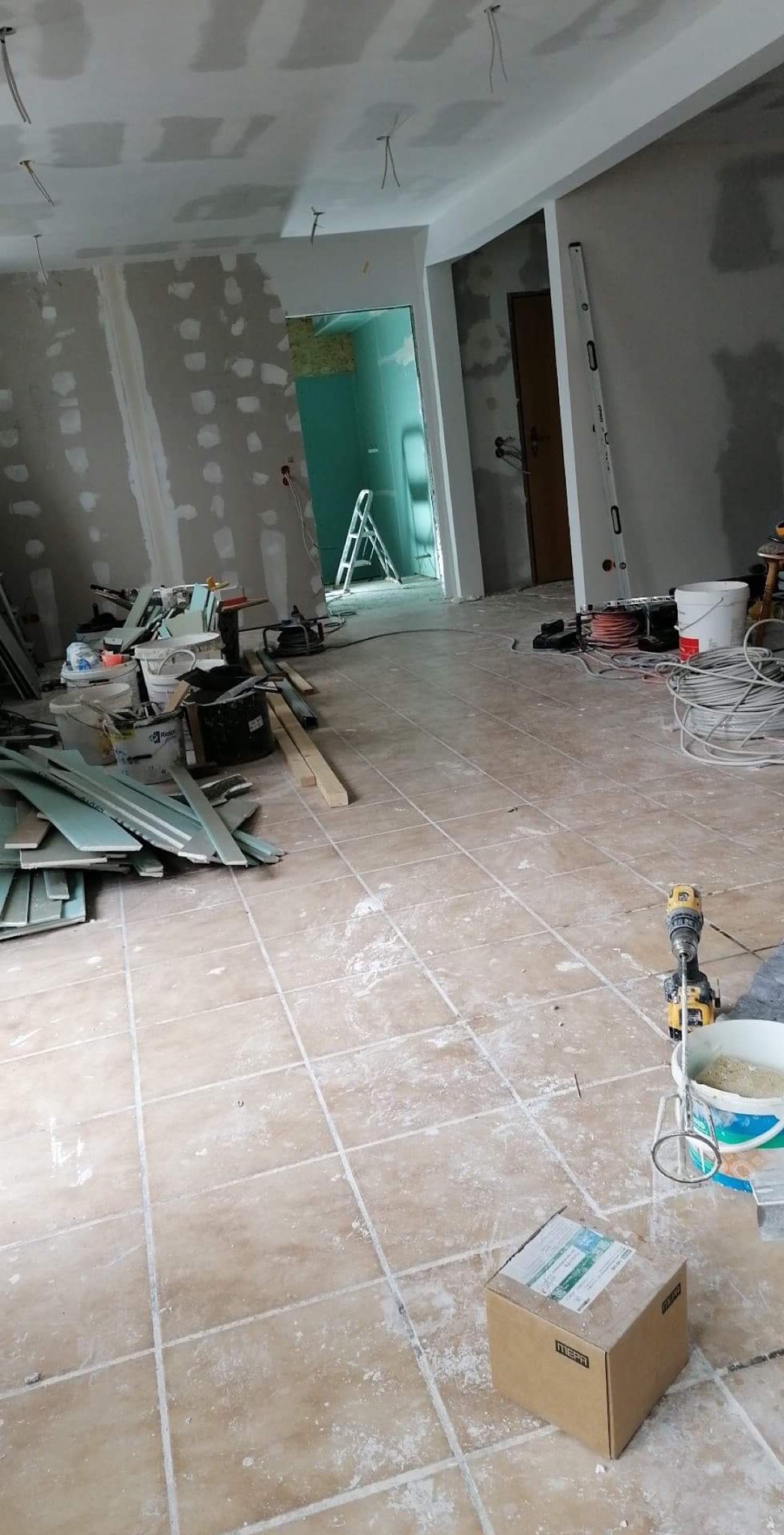 Wnętrze w trakcie remontu: ściany z płyt gipsowo-kartonowych przed wykończeniem, widoczne narzędzia i materiały budowlane, podłoga pokryta pyłem.