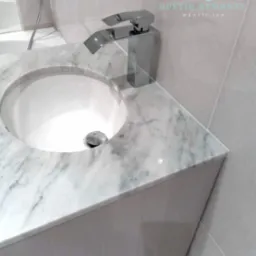 Umywalka nablatowa z marmurowym blatem i nowoczesną chromowaną baterią w minimalistycznej łazience, widoczne szare płytki na ścianie.