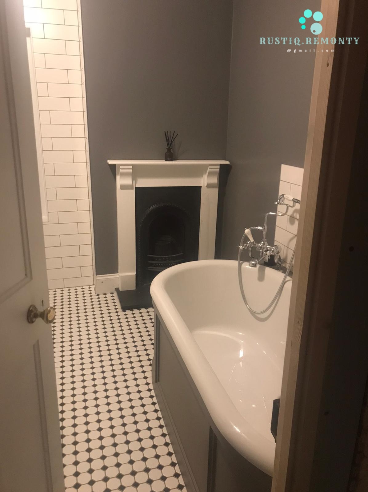 Przestronna łazienka w stylu wiktoriańskim z wolnostojącą wanną na tle ściany w kolorze grafitowym i kominkiem z białym obramowaniem. Podłoga wyłożona mozaiką w czarno-białe kropki, ściana...