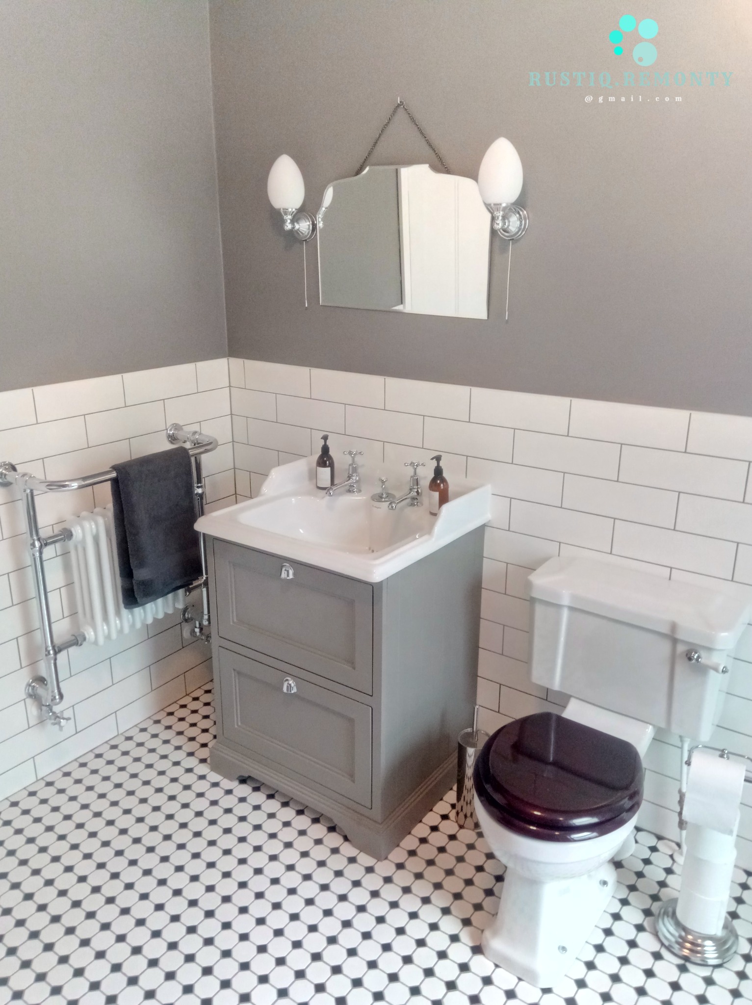 Klasyczna łazienka z szarą szafką pod umywalką, toaletą z ciemną deską, grzejnikiem drabinkowym i mozaikową podłogą w czarno-białe wzory.