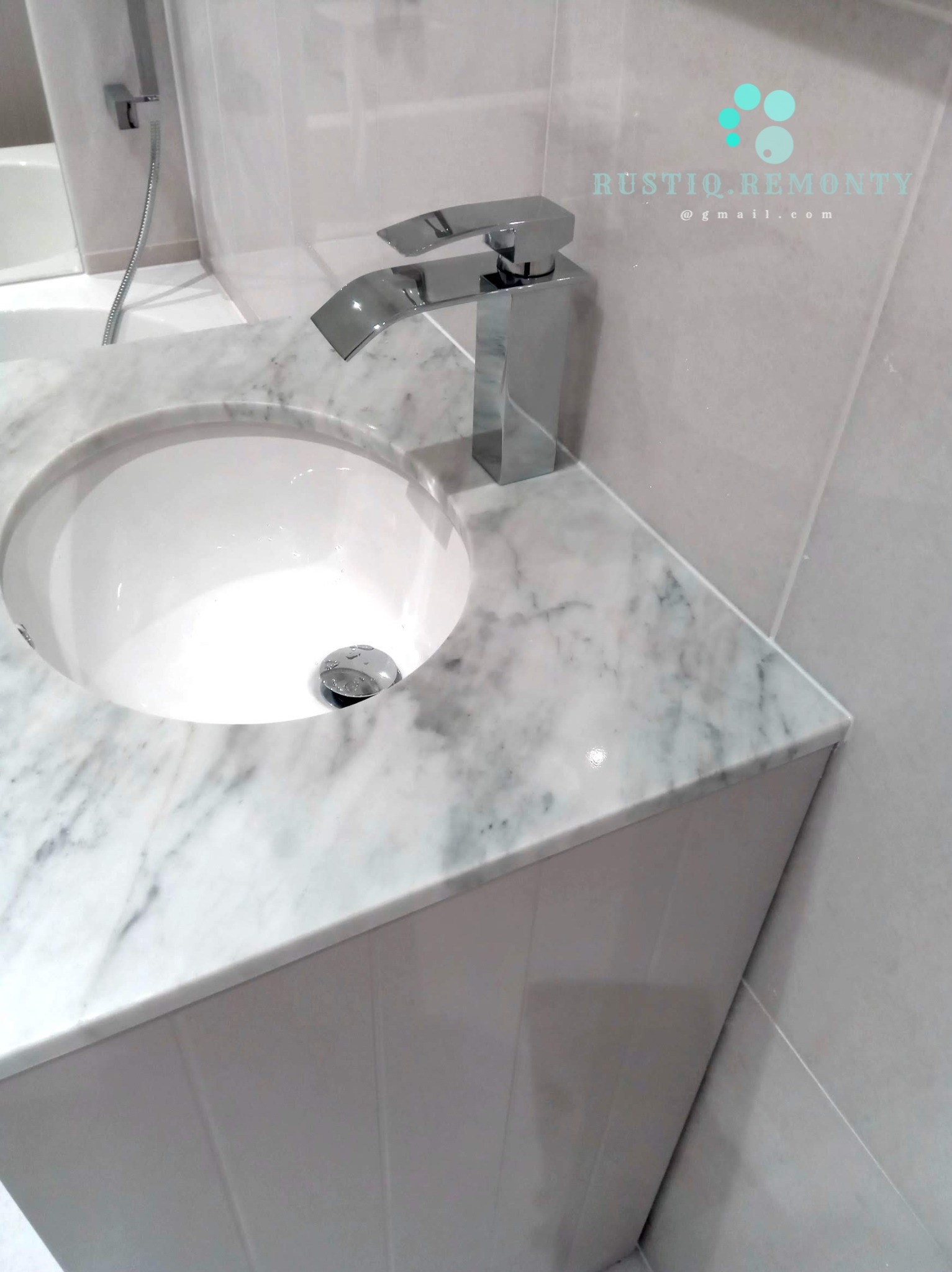 Umywalka nablatowa z marmurowym blatem i nowoczesną chromowaną baterią w minimalistycznej łazience, widoczne szare płytki na ścianie.