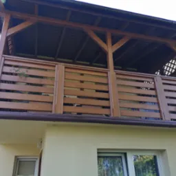 Zadaszony balkon z drewnianą balustradą z poziomych desek, widok z dołu, doniczkowe rośliny na balkonie, brązowe rynny.