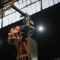 HOLE SP. Z O. O. - Profesjonalna kamera filmowa zamontowana na wysięgniku w studiu filmowym z widoczną konstrukcją oświetleniową w tle.