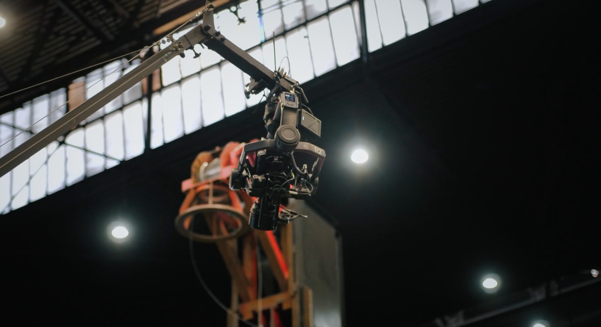 Profesjonalna kamera filmowa zamontowana na wysięgniku w studiu filmowym z widoczną konstrukcją oświetleniową w tle.
