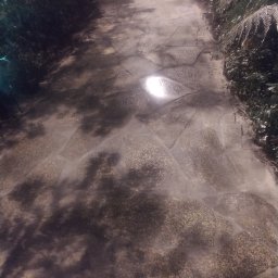 Adaśko firma budowlana - Ścieżka z nieregularnych kamieni w ogrodzie, z roślinnością po bokach i narzędziami w tle, oświetlona naturalnym światłem słonecznym.