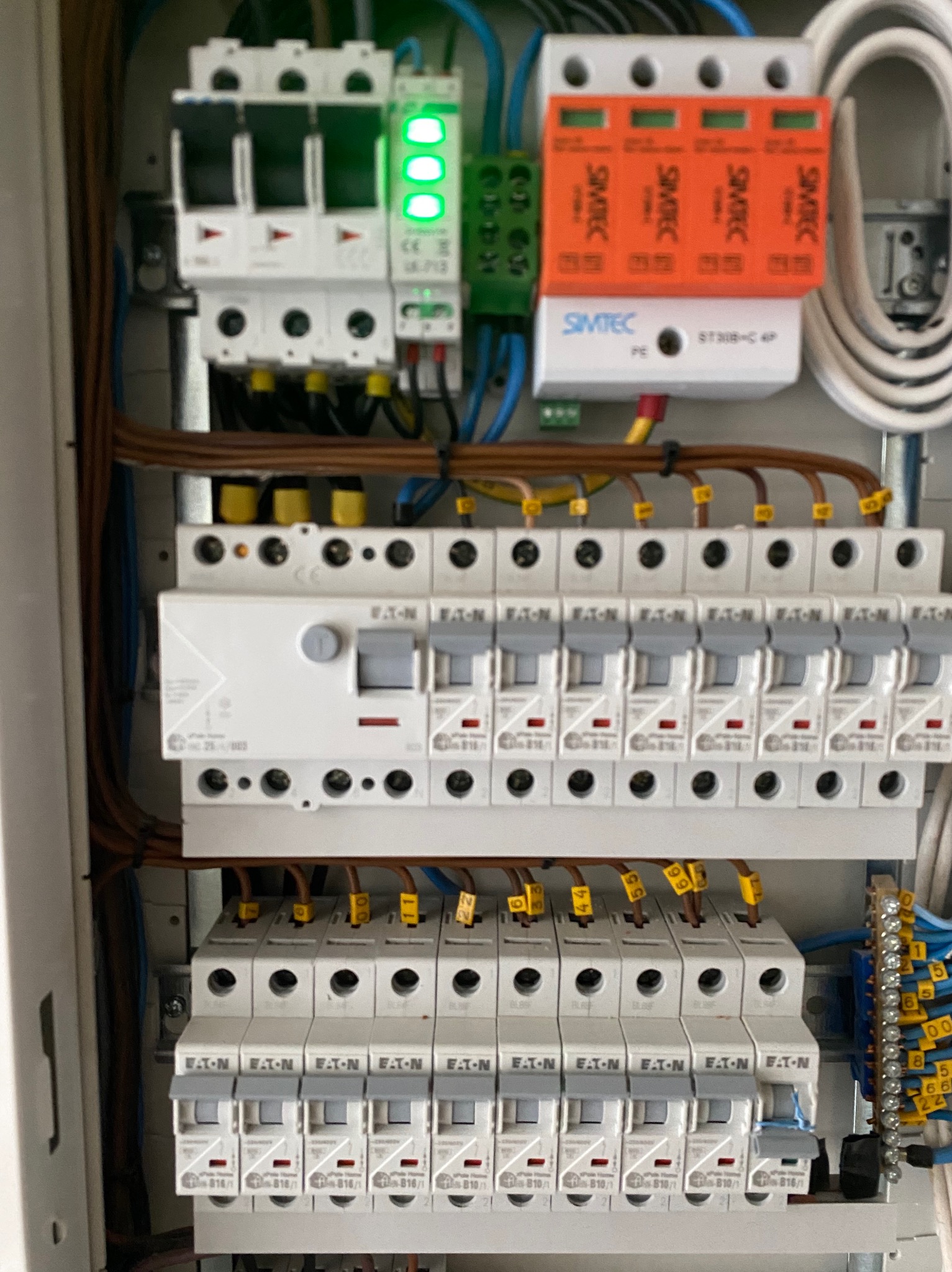 Rozdzielnica elektryczna z zainstalowanymi bezpiecznikami, ogranicznikiem przepięć Simtec i listwami zaciskowymi, widoczne kable z oznaczeniami.