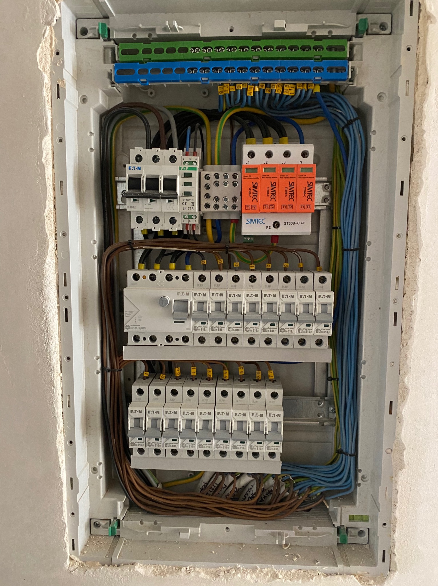 Rozdzielnica elektryczna z zainstalowanymi bezpiecznikami, zabezpieczeniami przepięciowymi SIMTEC, różnicówkami Eaton i listwami zaciskowymi, widok z bliska na elementy wewnątrz obudowy, po montażu...