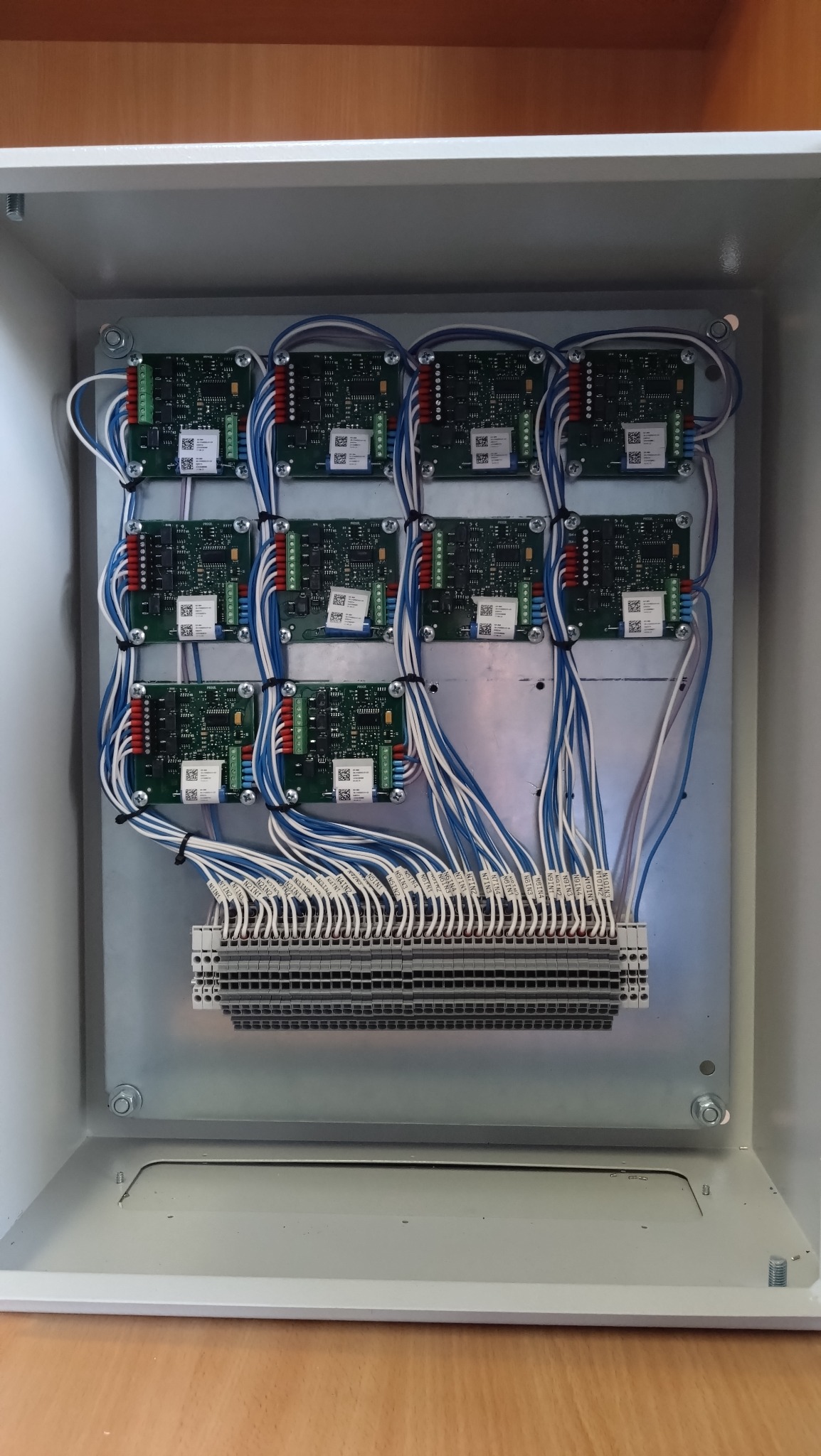 Rozdzielnica elektryczna wewnątrz metalowej obudowy z zamontowanymi modułami sterującymi i podłączonymi przewodami oznaczonymi etykietami.