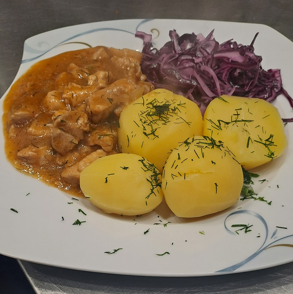 Danie na białym talerzu z sosem mięsnym, ziemniakami posypanymi koperkiem i surówką z czerwonej kapusty, widoczne delikatne zdobienie talerza.