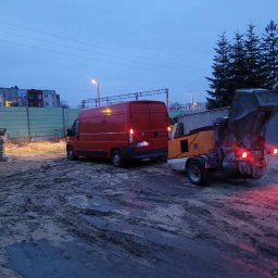 PRZEMYSŁAW PIOTRAK Alfa-Mix - Czerwony van z przyczepioną maszyną do wylewek na placu budowy, widoczne błoto i zapadający zmierzch.