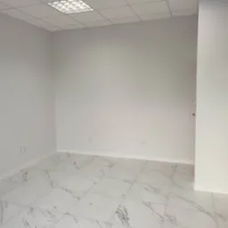 Pomalowane na jasnoszaro wnętrze biurowe z marmurową podłogą i zamontowanym oświetleniem sufitowym.