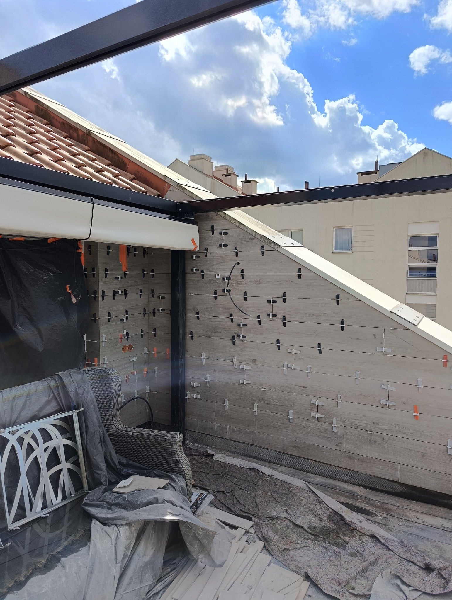 Montaż płytek imitujących drewno na elewacji tarasu, widoczne krzyżyki dystansowe i częściowo zasłonięte meble ogrodowe