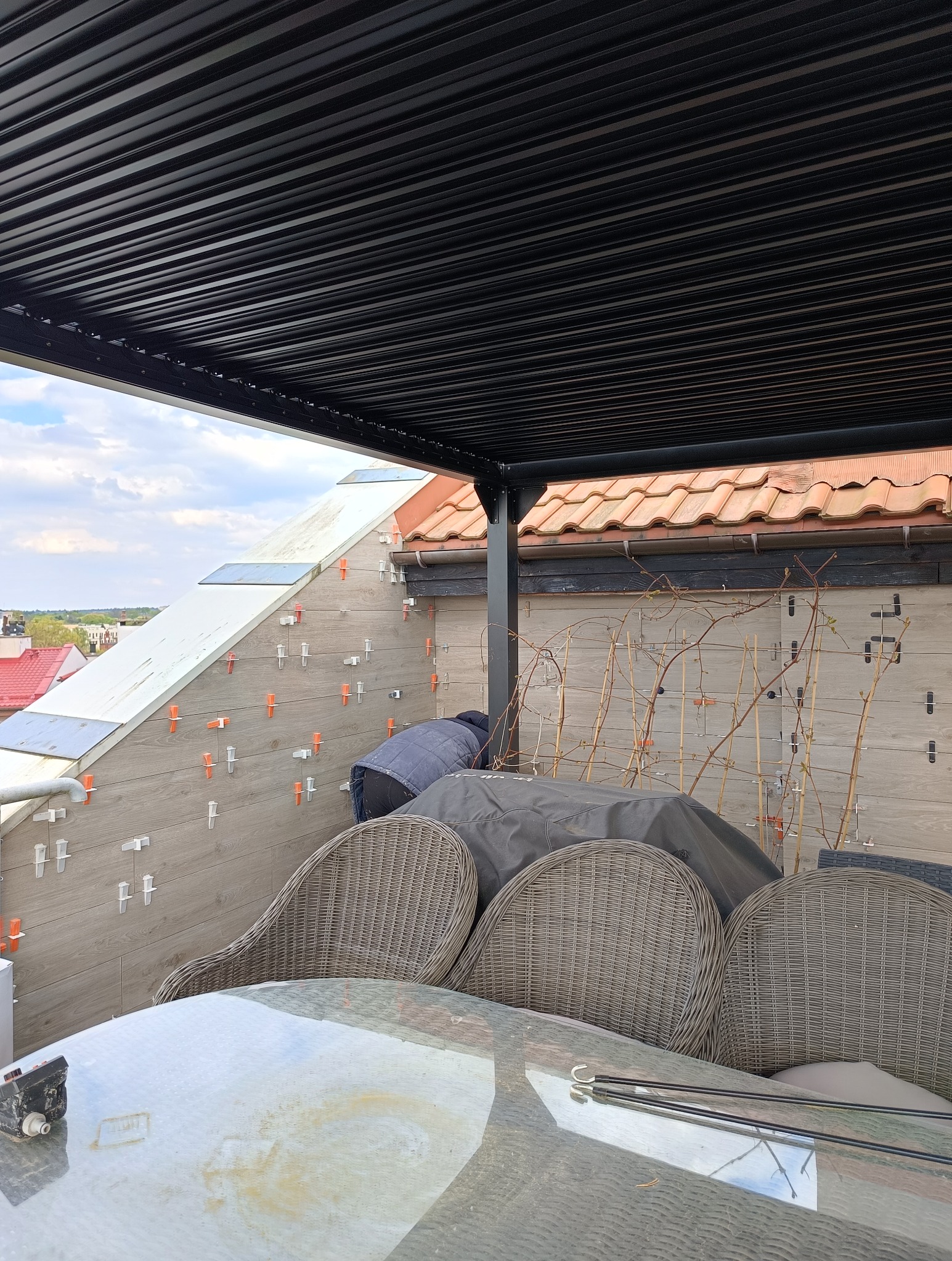 Montaż drewnopodobnych paneli ściennych na tarasie z użyciem klipsów dystansowych, widoczna czarna pergola i meble ogrodowe.