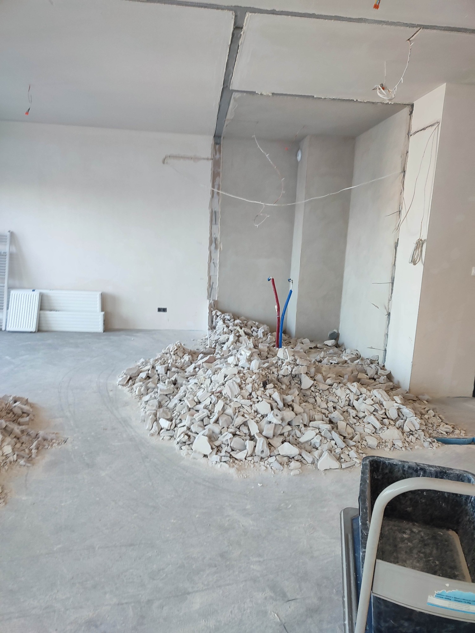 Stos gruzu po wyburzeniach na podłodze w trakcie remontu, widoczne wystające rury instalacji wodnej i odsłonięte przewody elektryczne