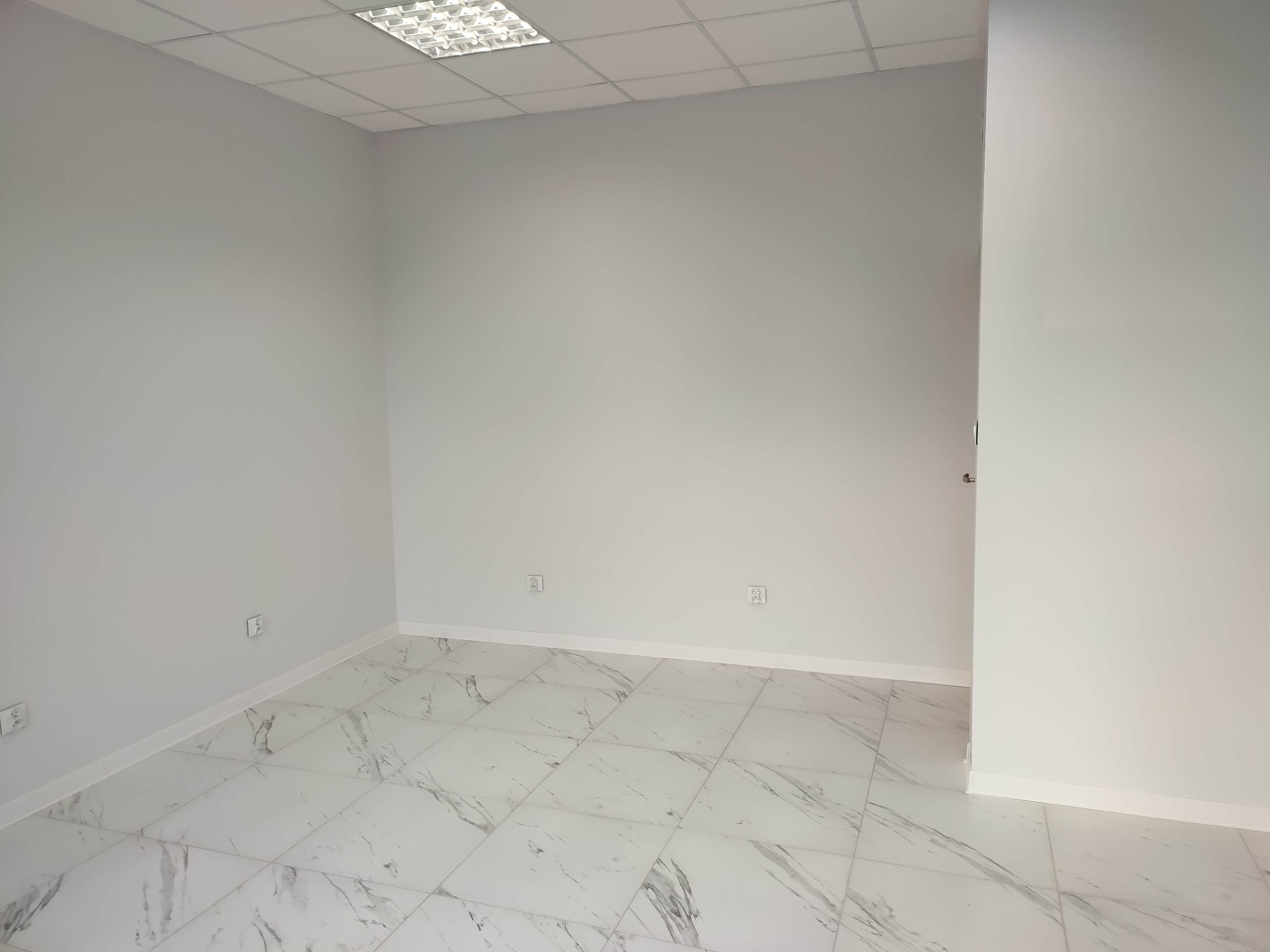 Pomalowane na jasnoszaro wnętrze biurowe z marmurową podłogą i zamontowanym oświetleniem sufitowym.
