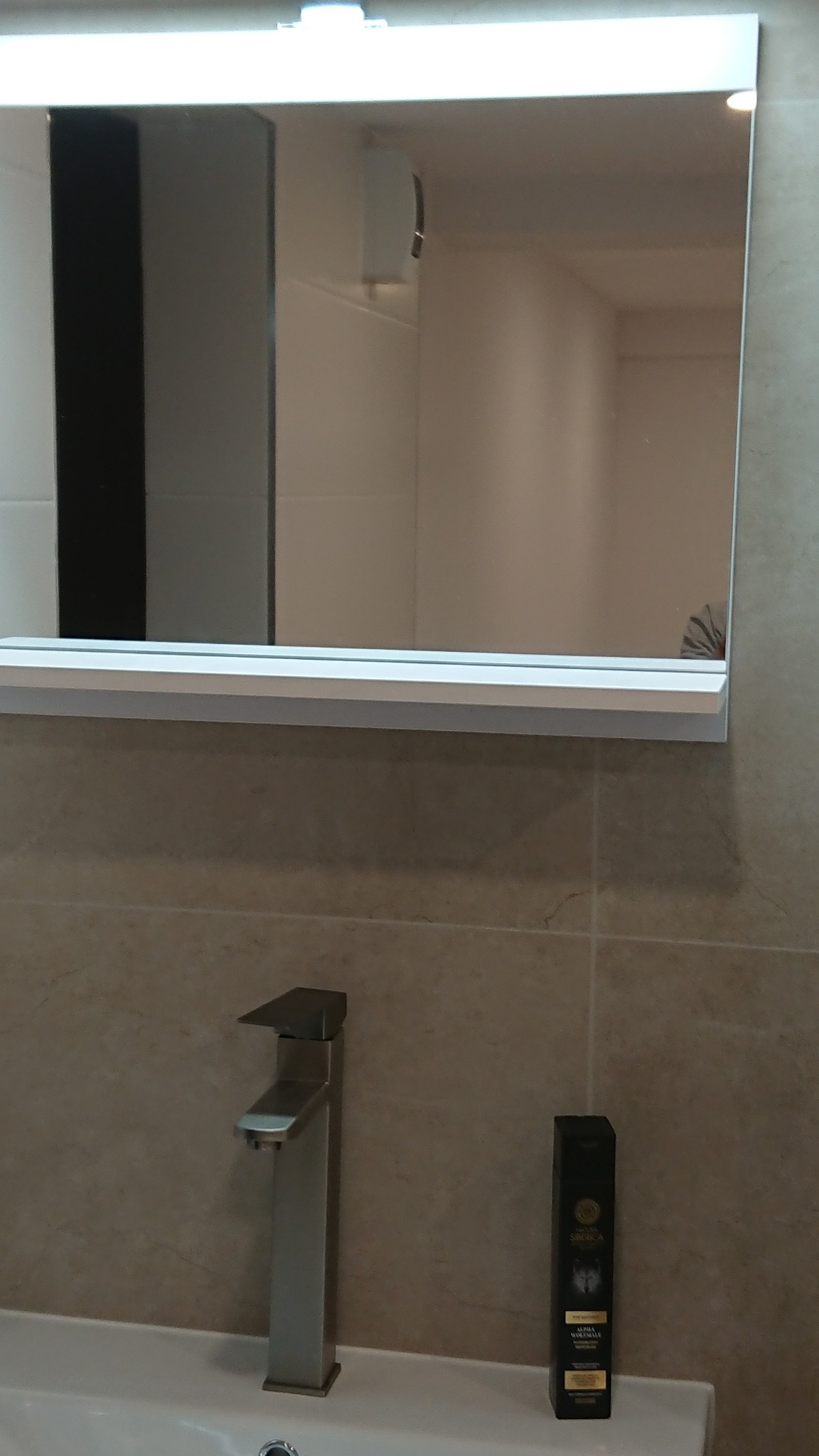 Nowoczesna łazienka z prostokątnym lustrem podświetlanym LED, chromowaną baterią umywalkową i kosmetykiem na blacie.