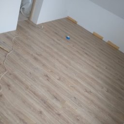 Wiesiek Jamniuk - Ułożone panele podłogowe w jasnym odcieniu drewna w pokoju. Widoczne narzędzia i listwy przypodłogowe. Usługa wykonana w Gorzowie Wielkopolskim.