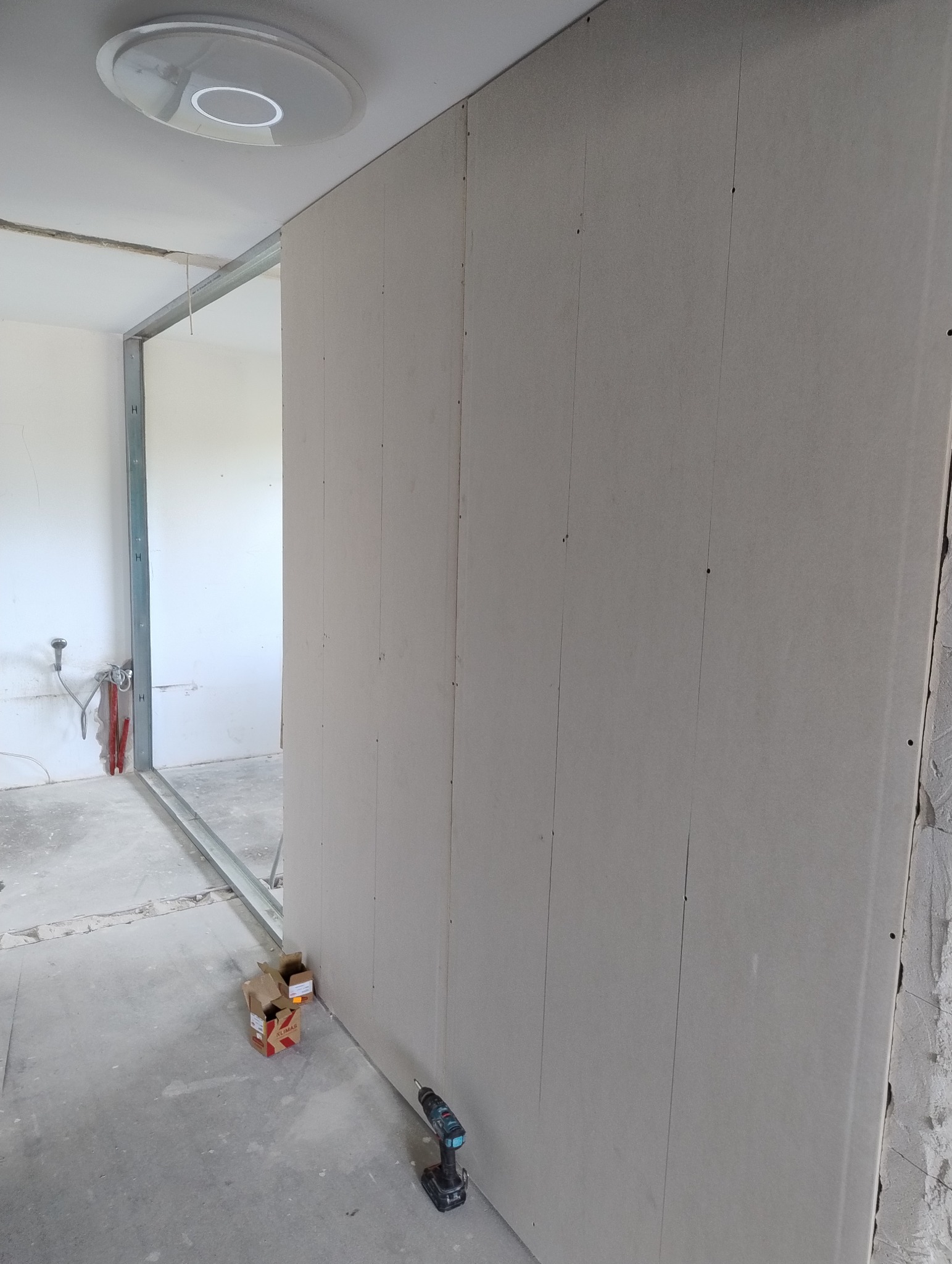 Montaż ścianki działowej z płyt gipsowo-kartonowych. Widoczne profile, płyty, wkrętarka i karton po wkrętach. W tle instalacja wodna.