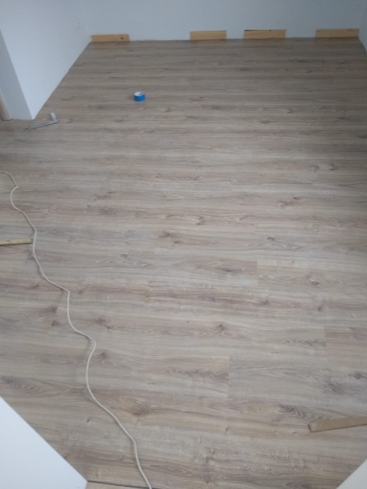 Ułożone panele podłogowe w pokoju, widoczne listwy przypodłogowe i kabel. Nowa podłoga z jasnego drewna z widoczną strukturą.