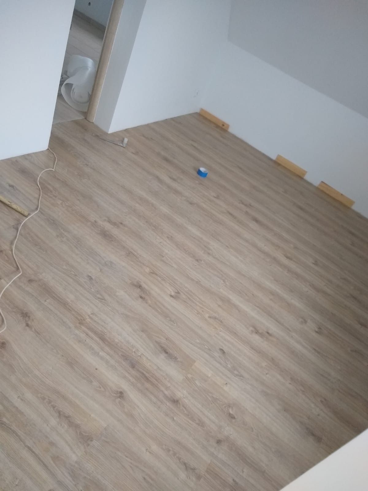 Ułożone panele podłogowe w jasnym odcieniu drewna w pokoju. Widoczne narzędzia i listwy przypodłogowe. Usługa wykonana w Gorzowie Wielkopolskim.