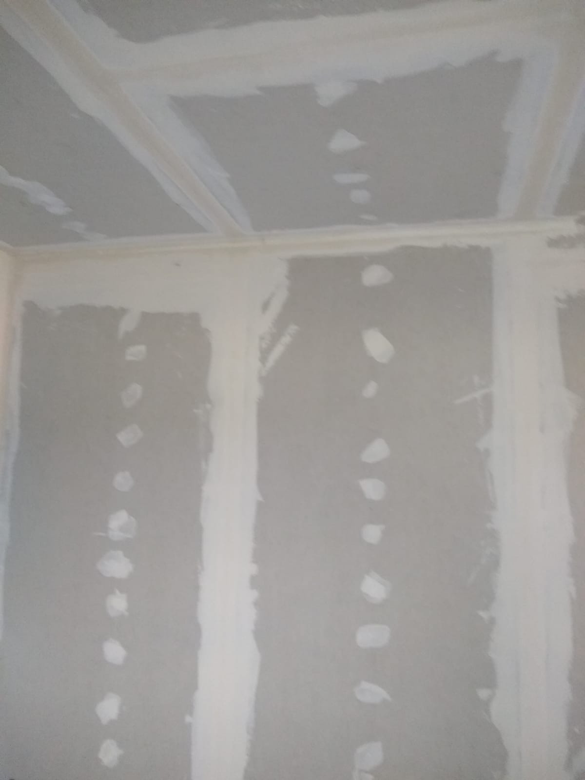 Szpachlowana ściana i sufit z widocznymi łatami gipsowymi i wypełnionymi łączeniami, przygotowane do dalszych prac wykończeniowych.