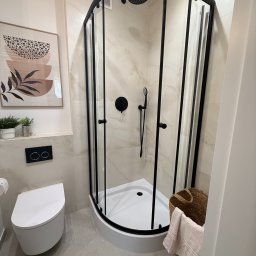 ITD. Usługi Budowlane - Nowoczesna łazienka z kabiną prysznicową z czarnymi profilami, podwieszaną toaletą i dekoracjami w beżowej tonacji.