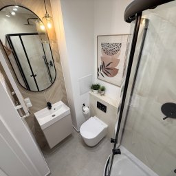 ITD. Usługi Budowlane - Nowoczesna łazienka z owalnym lustrem, kabiną prysznicową z czarnymi detalami i minimalistyczną umywalką. Uwagę zwraca plakat z motywem roślinnym i geometrycznym.