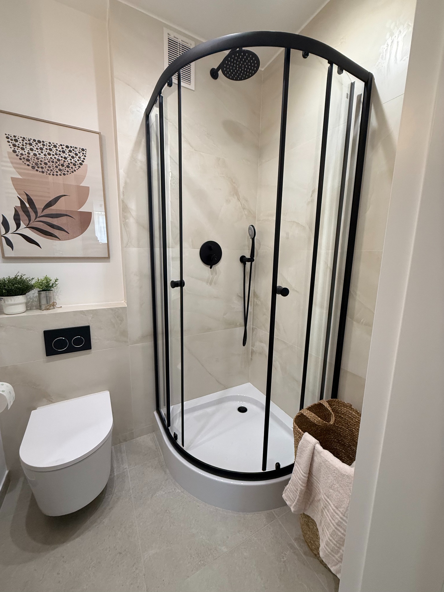 Nowoczesna łazienka z kabiną prysznicową z czarnymi profilami, podwieszaną toaletą i dekoracjami w beżowej tonacji.