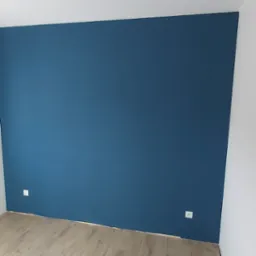 Ściana pomalowana na ciemny niebieski kolor w Namysłowie, widoczne gniazdka elektryczne i fragment podłogi laminowanej.